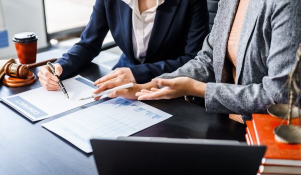 Two,Female,Lawyers,In,Business,Suits,Meet,At,Wooden,Desk,